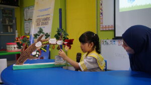 Seorang siswa sedang menjelaskan daur hidup kupu-kupu melalui proyek yang dibuatnya