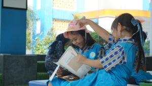 Senyum ceria siswa putri terbit ketika sedang membaca buku pilihannya