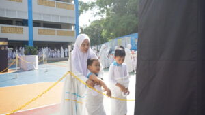 Dengan bimbingan seorang teacher, siswa melempar kerikil ke salah satu jamrah