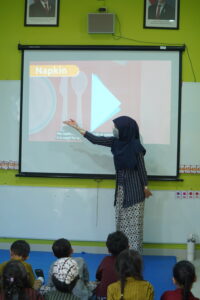 Ms. Erza, teacher grade Kindy-2, sedang memberikan penjelasan mengenai praktik table manner