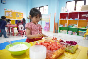 Seorang siswa sedang memilih buah-buahan untuk dimasukkan ke dalam mangkuk saladnya