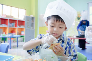 Dengan penuh kehati-hatian, seorang siswa memasukkan irisan sayur ke dalam tahu